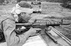 Pfc. Ron Fuller of Indianapolis, Ind., his head bandaged after being hit by shrapnel and his AR-15 at the ready, watches for the enemy from atop an armored personnel carrier.