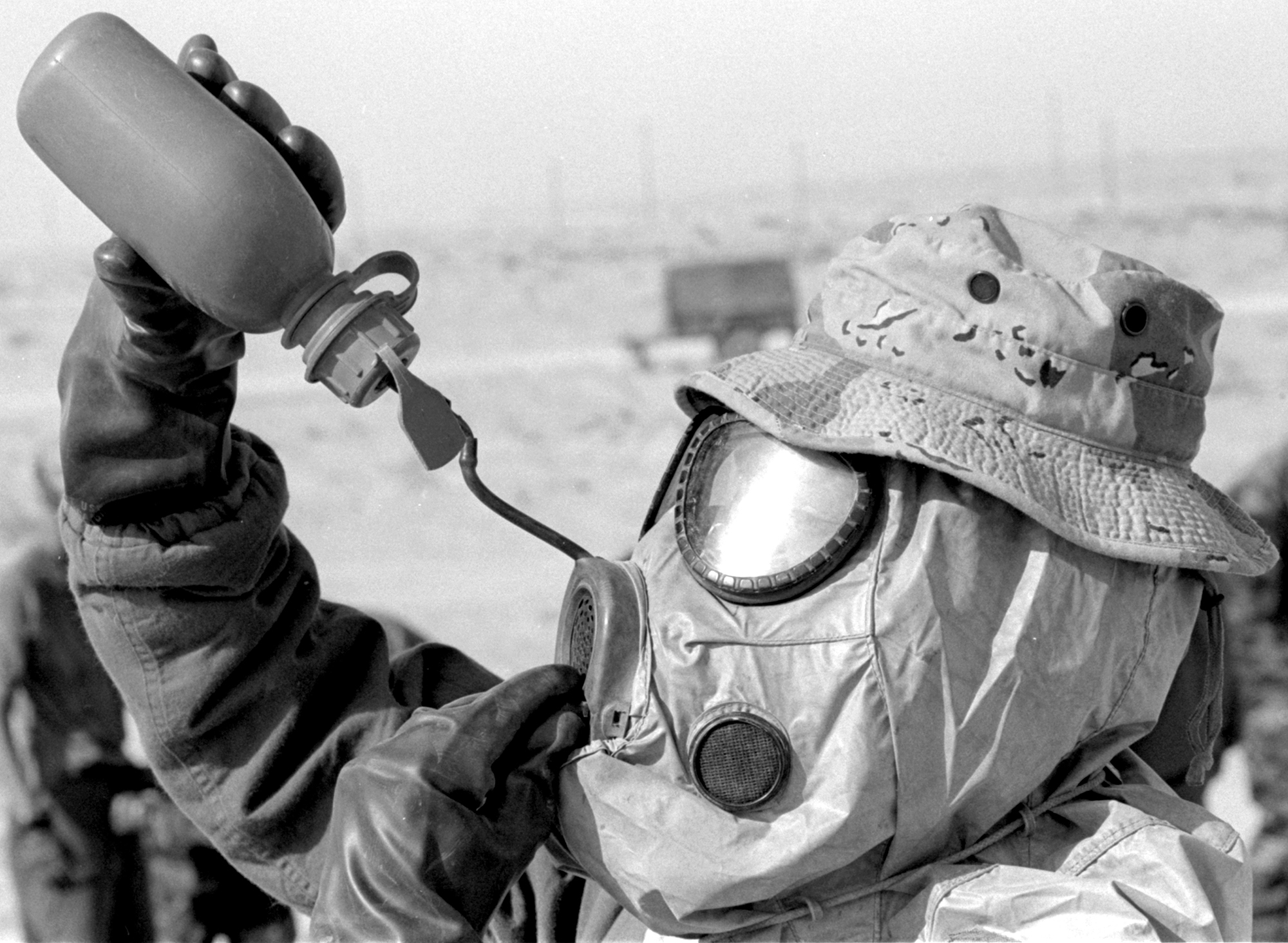 A U.S. Marine taking part in a chemical decontamination exercise in the weeks before the Gulf War gets some relief from the heat of his protective gear and the Saudi Arabian desert.
