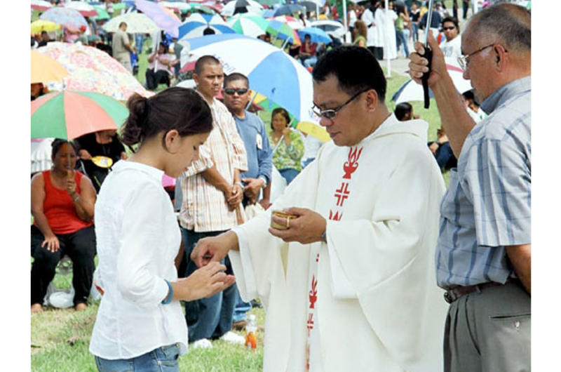 Marissa Laracuente, 11, receives Holy Communion from Father Carl Vila during the All Souls Day Mass on Wednesday in the Guam Veterans Cemetery.