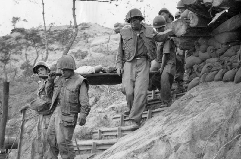 A wounded "buddy" is carefully carried down the ragged hill on his way to the rear for medical care.