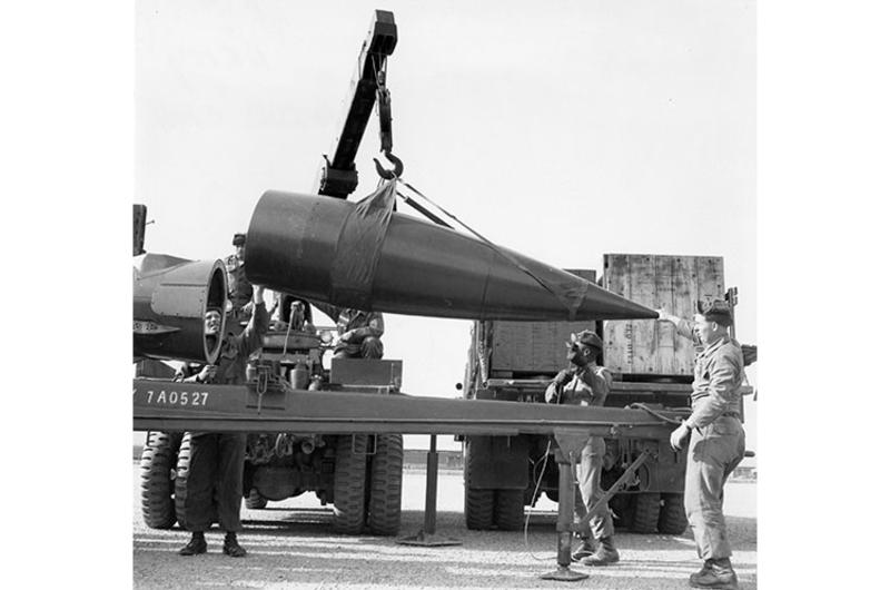 Members of a missile battery of the 4th U.S. Missile Command load the warhead of an Honest John missile onto its launch pad with the help of a crane.