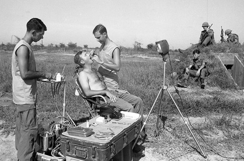 Field dentist clamp down in Vietnam. Dr. (dentist, Captain) Earle Yeamans and assistant Sp5 Richard Ackley (wearing glasses, on left) treat an 1st Infantry Division infantryman "on the scene" at a 1st Infantry Division defensive perimeter.