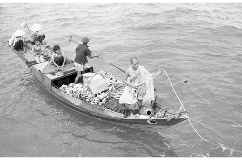 Swift boat stops sampan on way to market. Yellow-robed buddhist monk sits in bow.