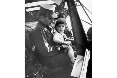 Miller with young Donny; Korean orphan heads for home in Indiana. Big-eyed little Donny stares out of the cockpit as he sits on his adoptive father's lap.
