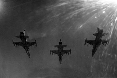 F5 "Falcon" fighter jets of the 522nd Fighter Squadron of the South Vietnamese air force fly through the air on a bombing mission, the jets sillouhetted agains the sun.